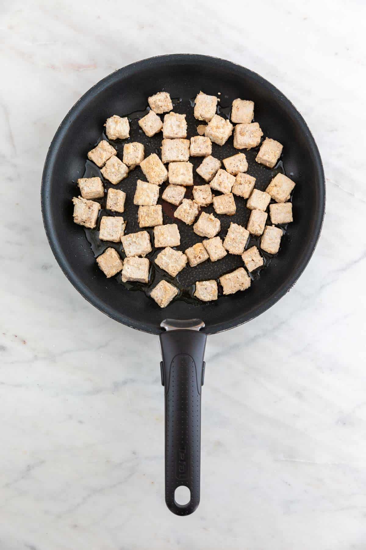 Tofu cubes on a non-stick frying pan with some oil while cooking.