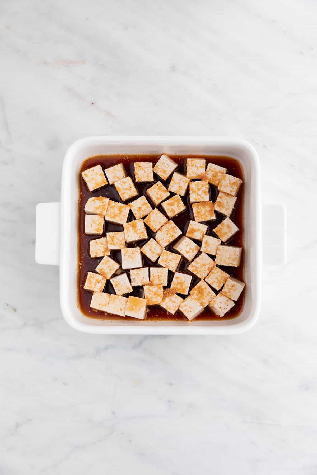 Tofu cubes in a shallow dish with the marinade liquid.