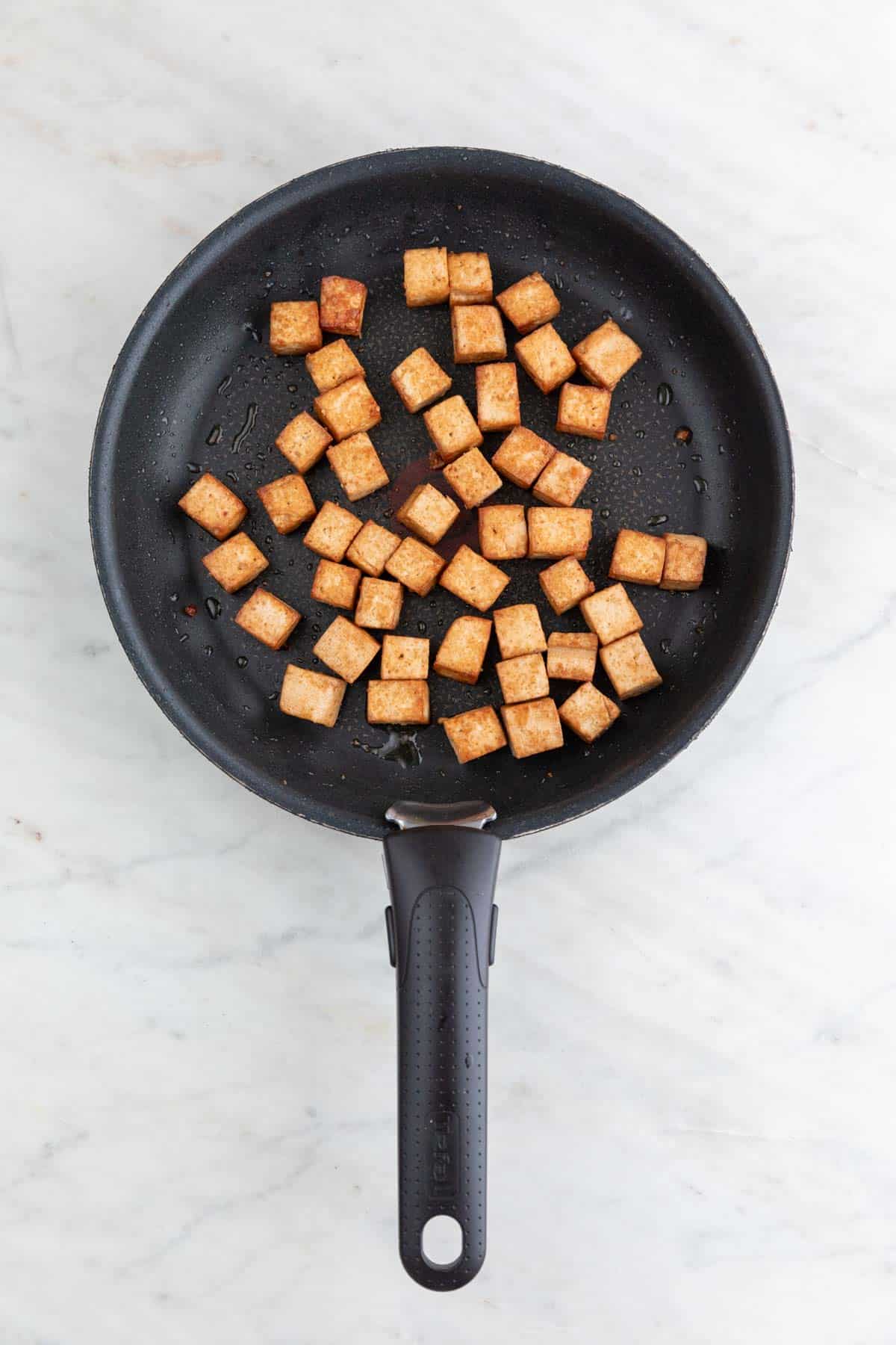 Marinated tofu cubes cooked in a non-stick pan.