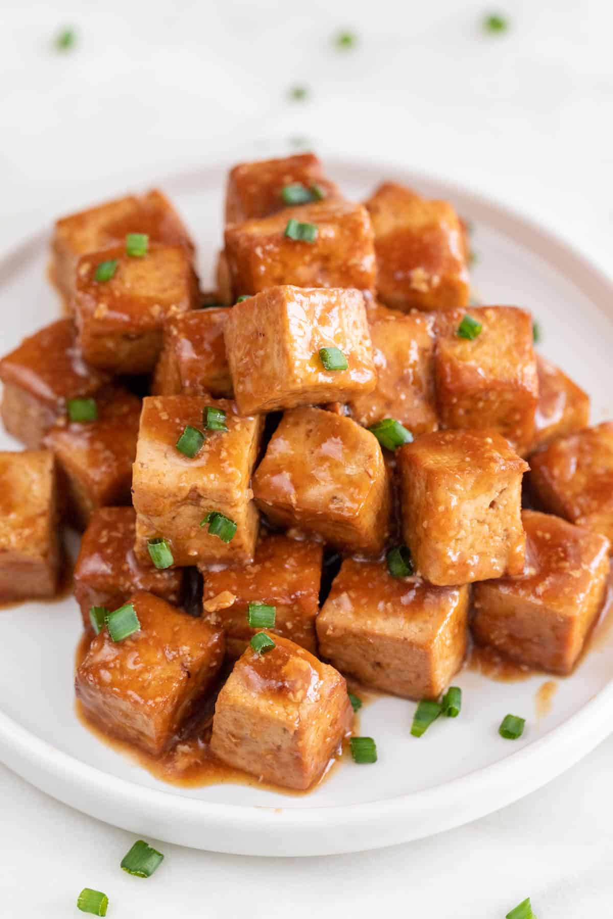 Marinated tofu cubes in a dish with some chopped chives on top.