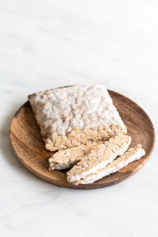 A sliced block of tempeh onto a wooden plate.