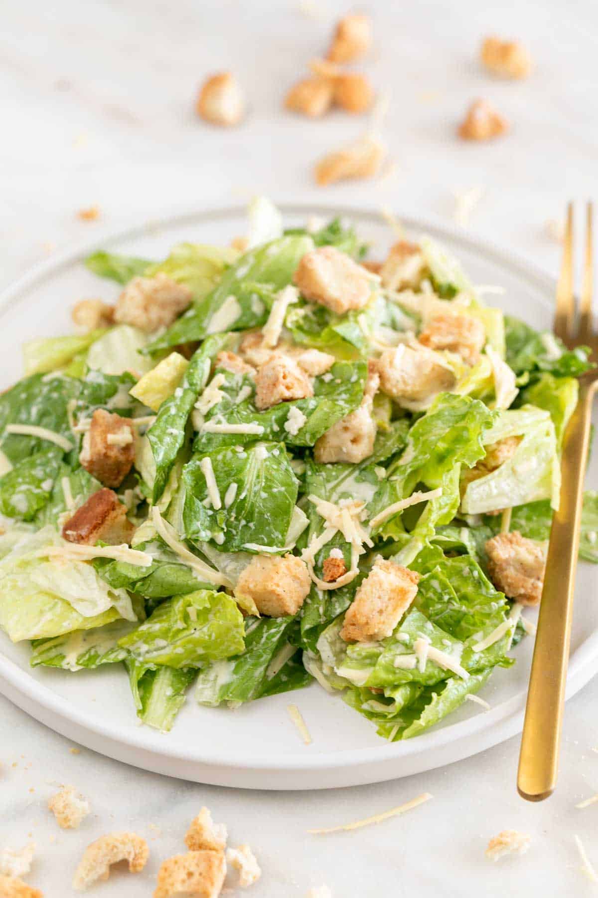 Vegan Caesar salad on a plate with a fork and croutons in the background.
