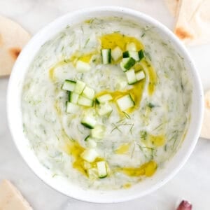 Bowl of vegan tzatziki sauce garnished with cucumber and olive oil.