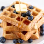 A tower of fluffy vegan waffles topped with blueberries, vegan butter, and maple syrup.