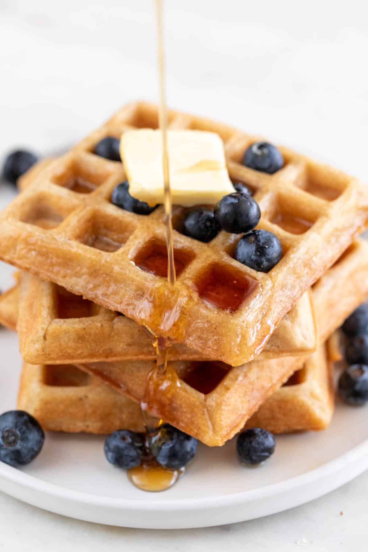 Stacked vegan waffles with blueberries, vegan butter, and maple syrup drizzle.