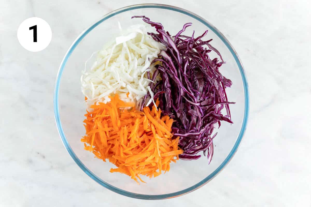 Large mixing bowl with finely shredded green cabbage, red cabbage and carrot.