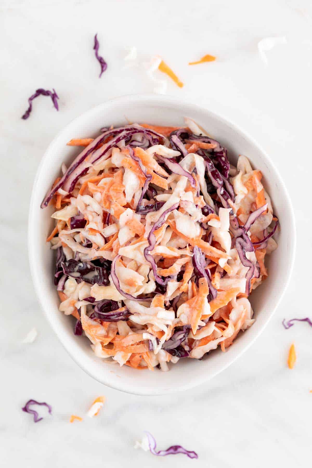 White bowl with vegan coleslaw surrounded by vegetables.