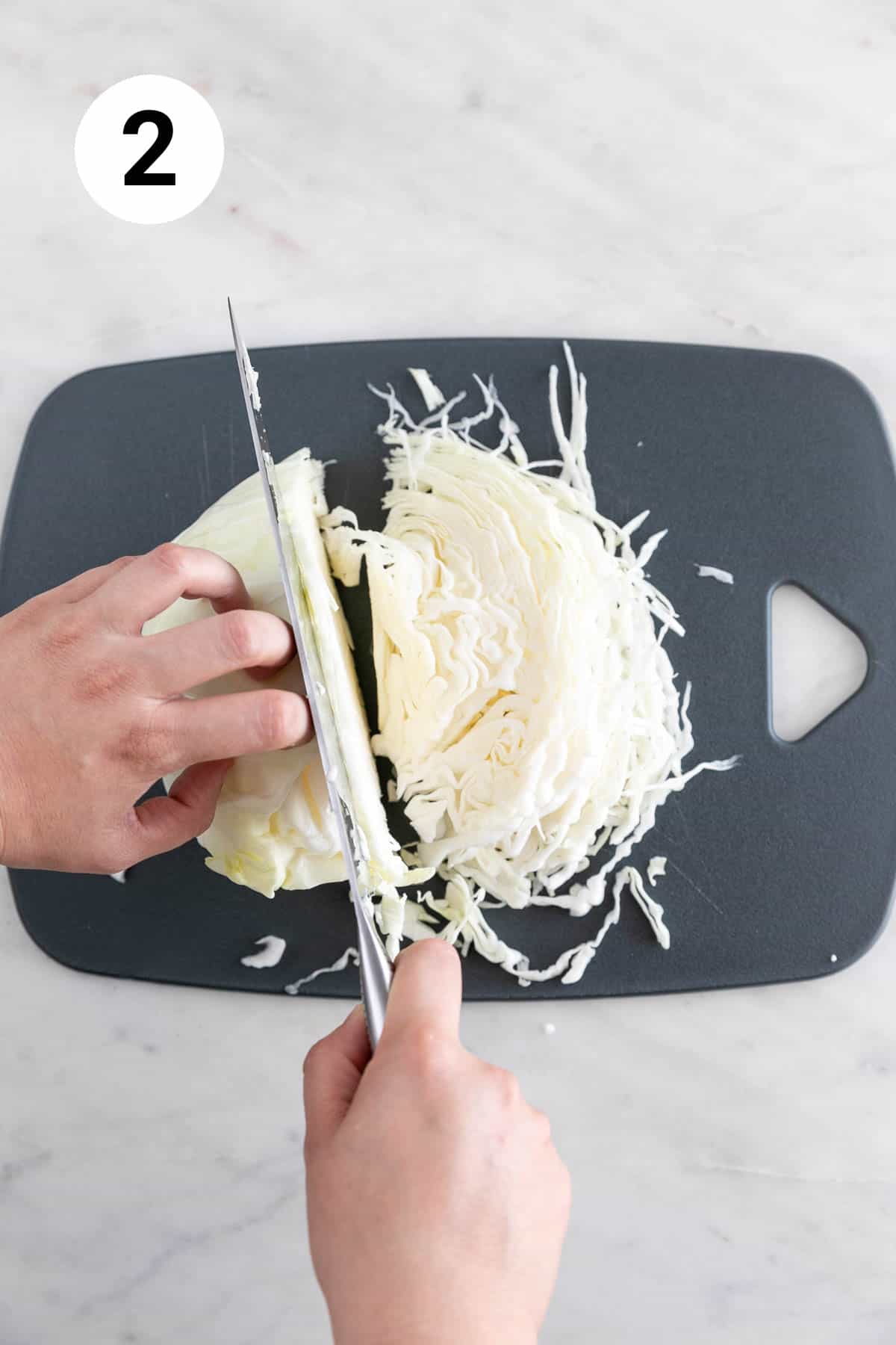 Hands finely chopping cabbage on a cutting board.