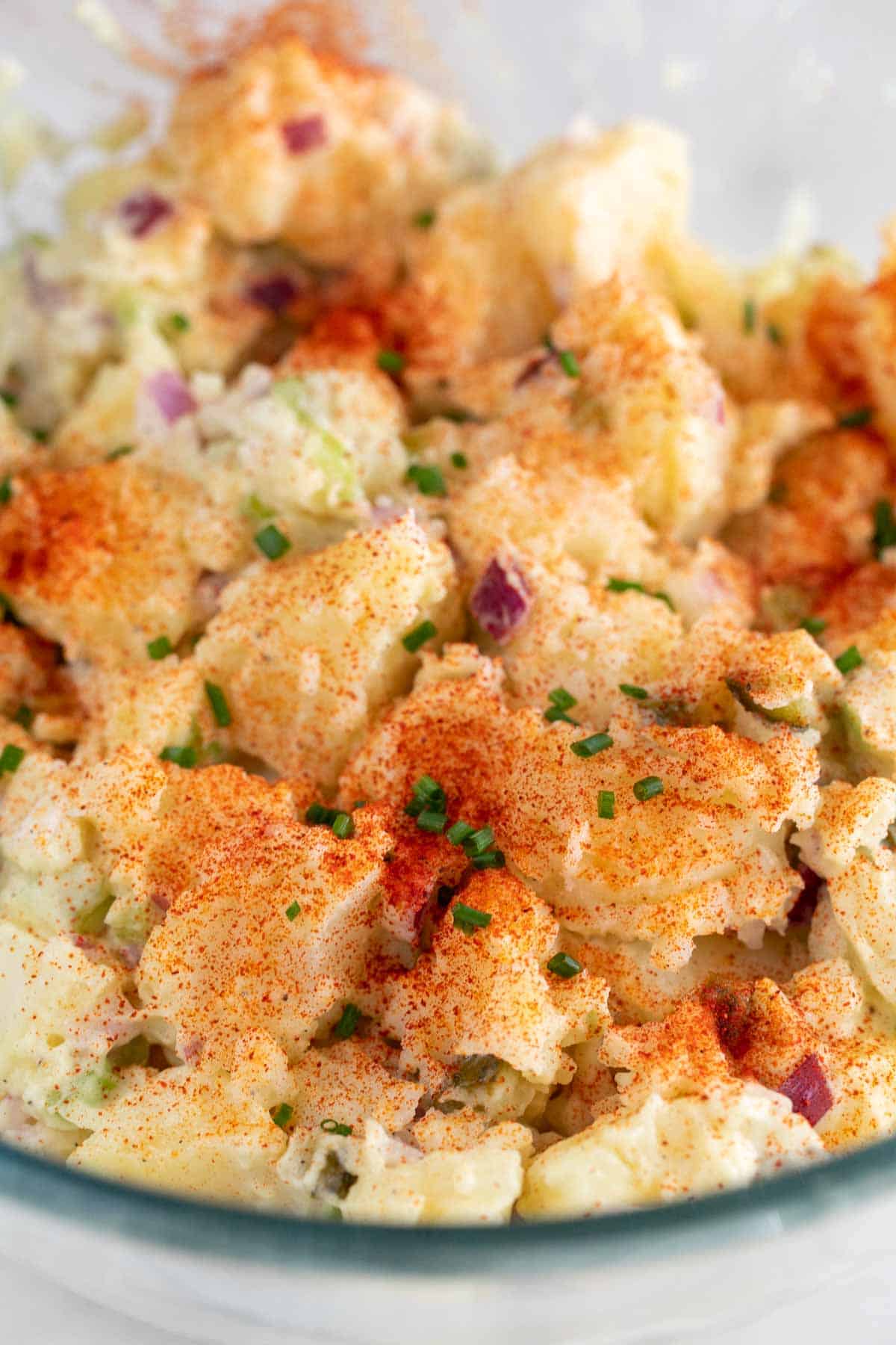 A bowl of vegan potato salad with a sprinkle of paprika and chives on top.