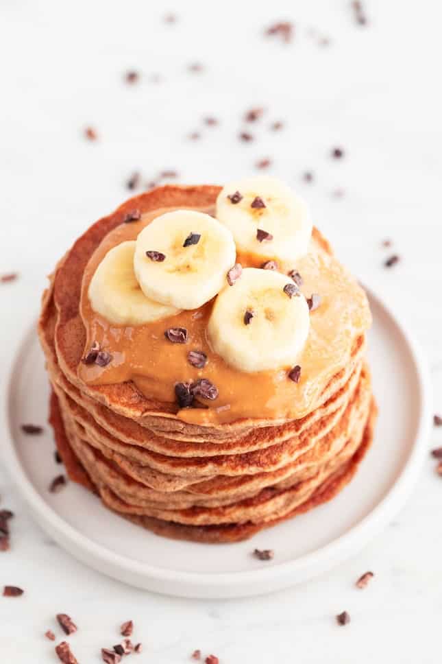 Vegan banana pancakes stacked with peanut butter, chocolate chips, and banana slices.