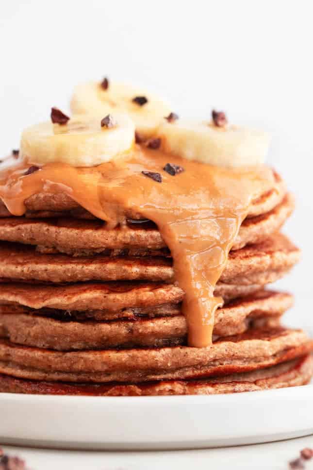 Vegan banana pancakes stack with peanut butter, chocolate chips, and sliced banana.