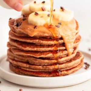 Vegan banana pancakes topped with peanut butter, chocolate chips, and sliced bananas.