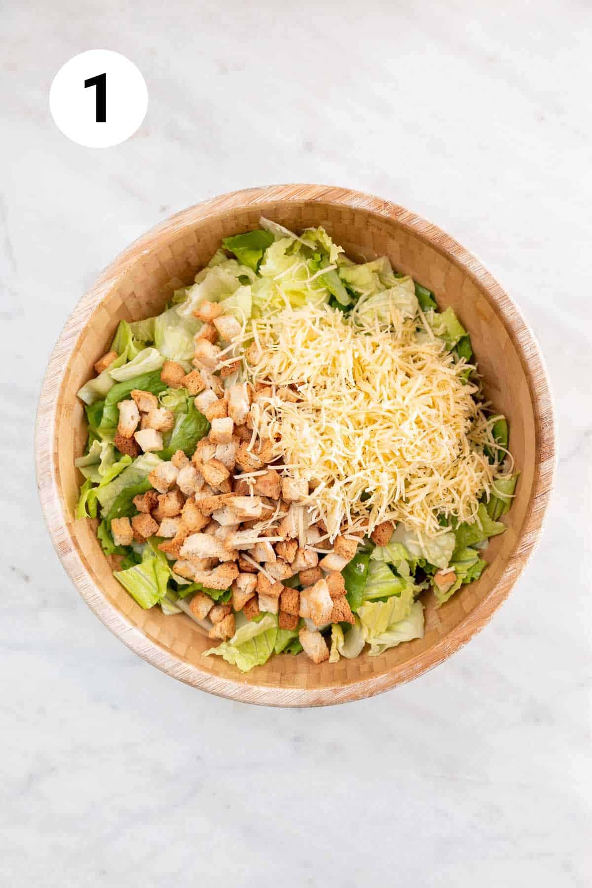 Romaine lettuce, vegan cheese, and croutons arranged in a large mixing bowl.