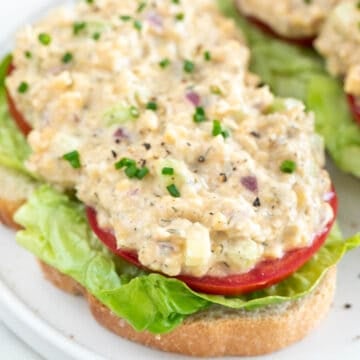 Sliced bread topped with lettuce, tomato, and vegan chicken salad.