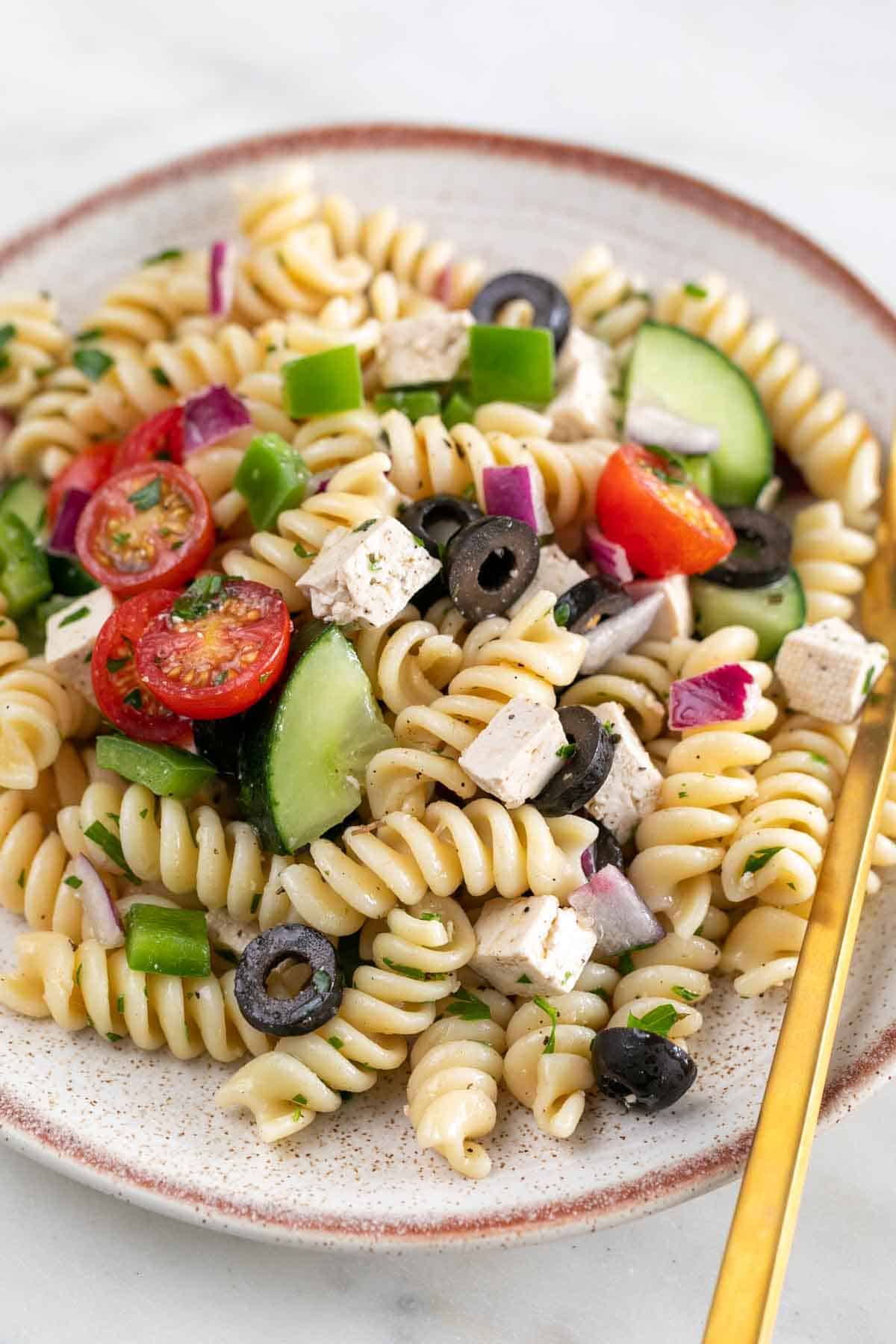 Serving of vegan pasta salad in a shallow dish, accompanied by a fork.