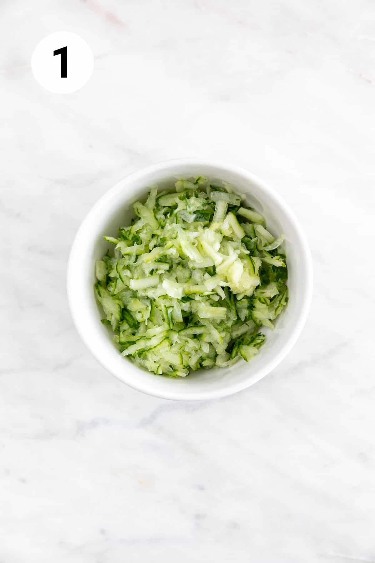 Grated cucumber in a white bowl.