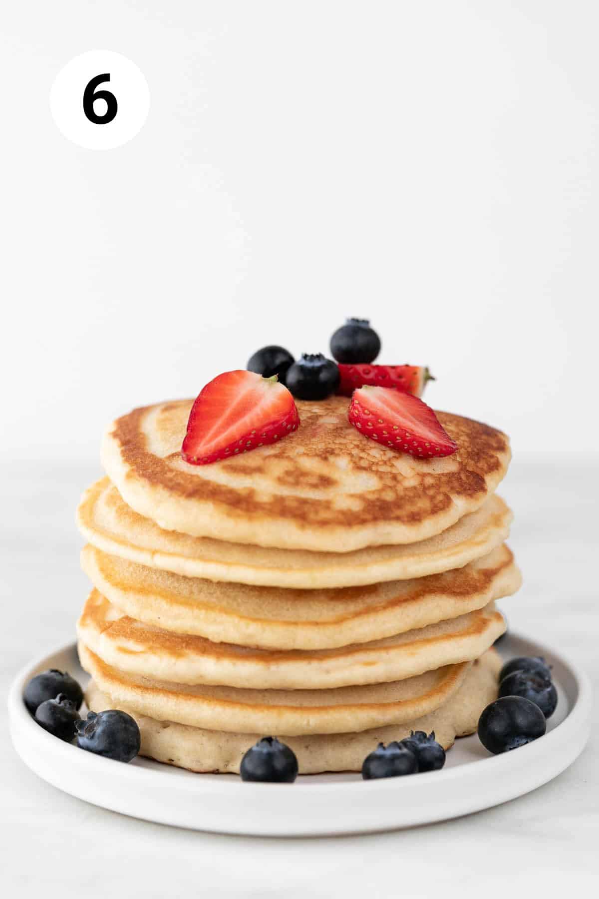 Stack of vegan pancakes topped with fresh strawberries and blueberries.