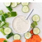 A bowl of vegan ranch dressing, a spoon, and a variety of crudités nearby.