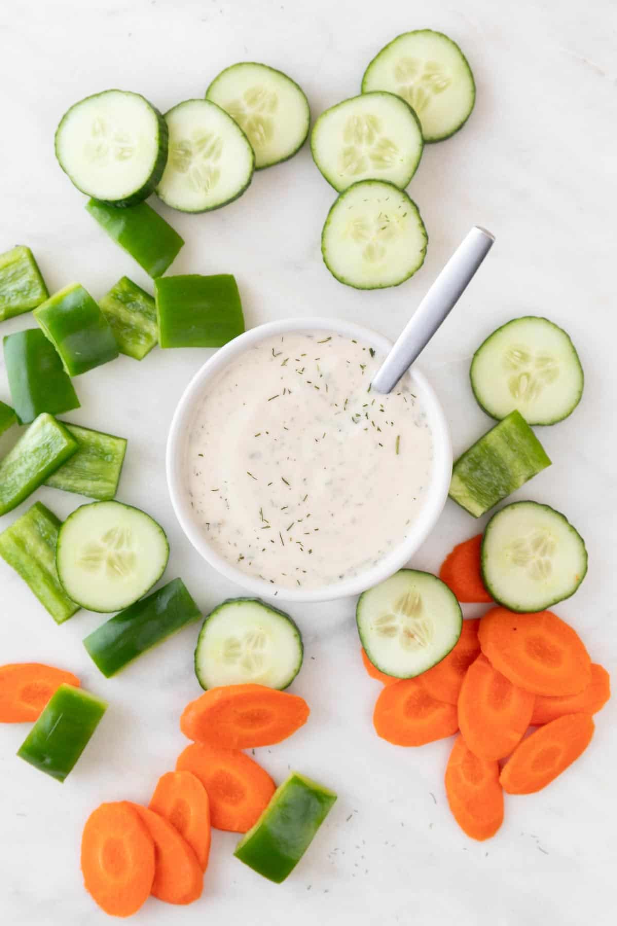 A bowl of vegan ranch dressing with a spoon, surrounded by crudités.