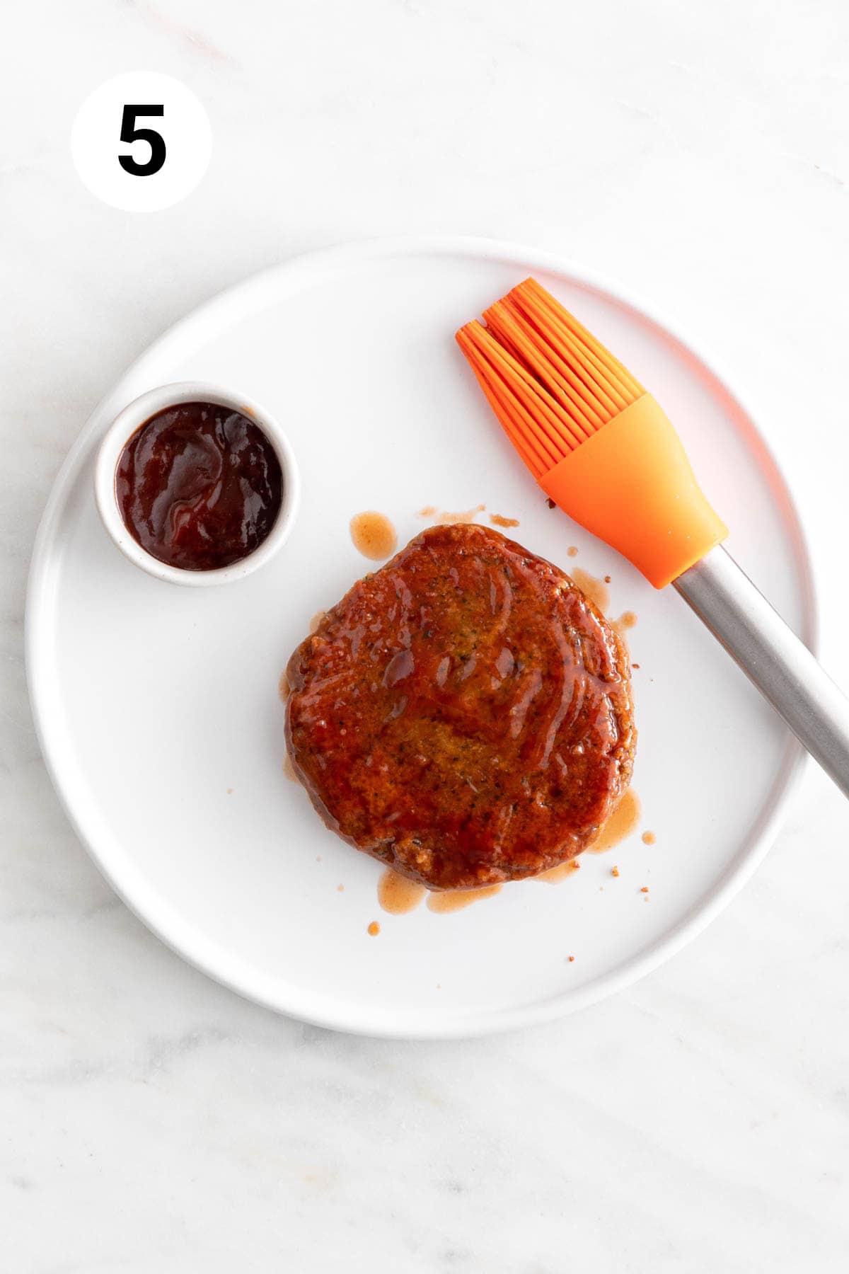 A vegan chickpea burger brushed with BBQ sauce on a white plate.