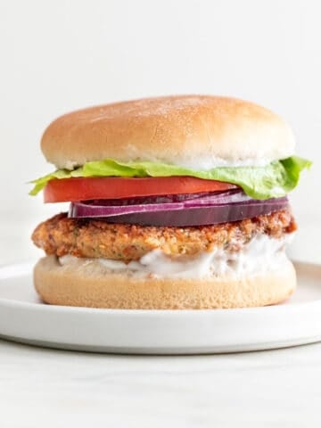 On a white plate, a vegan chickpea patty on a bun with lettuce, tomato, red onion, and mayo.