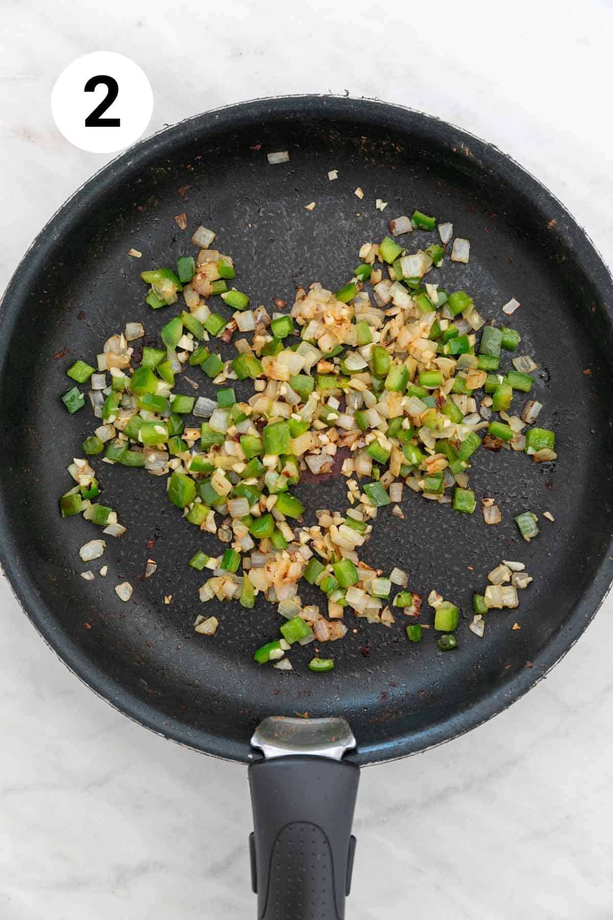 Onion, green bell pepper, and garlic cooked in a skillet.