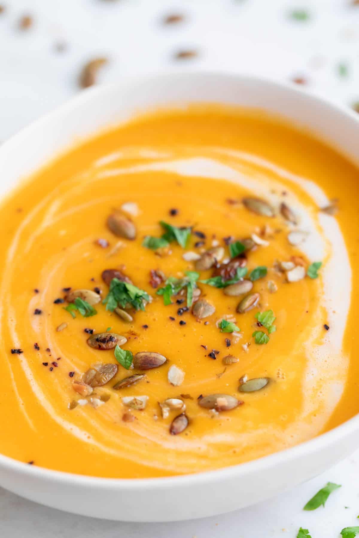 Bowl of vegan pumpkin soup garnished with parsley, coconut milk, and black pepper.
