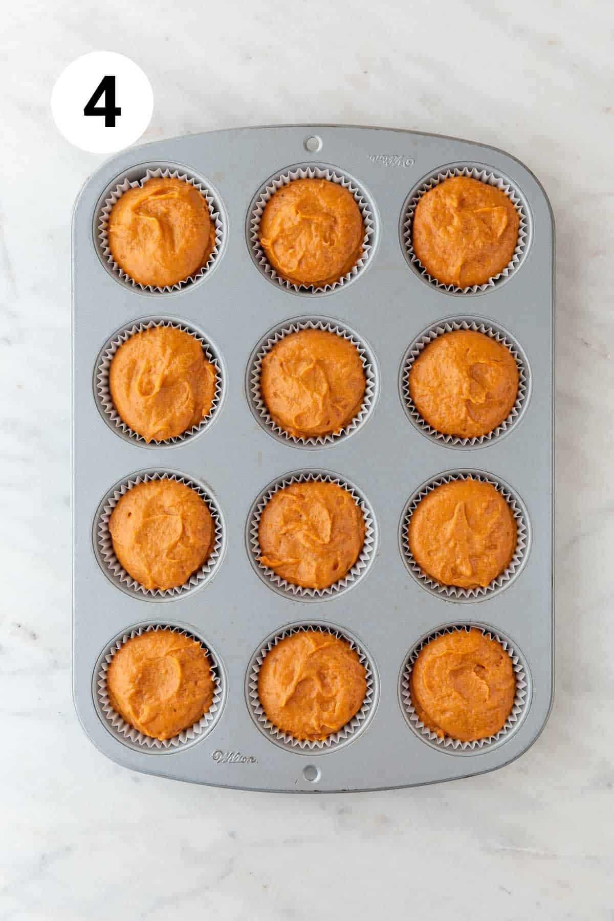 Muffin pan with liners filled with vegan pumpkin muffin batter.