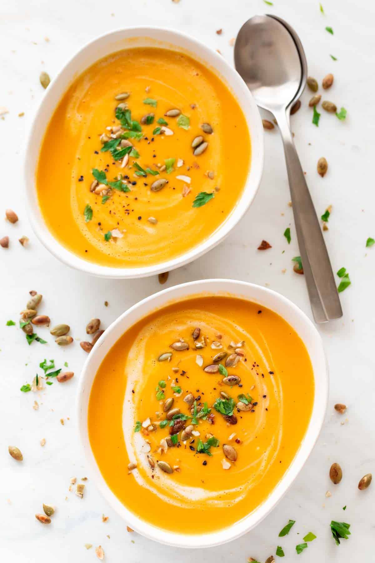 Two bowls of vegan pumpkin soup, each garnished with coconut milk, parsley, and black pepper.