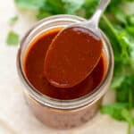 Spoonful of red enchilada sauce resting on a jar of red enchilada sauce.