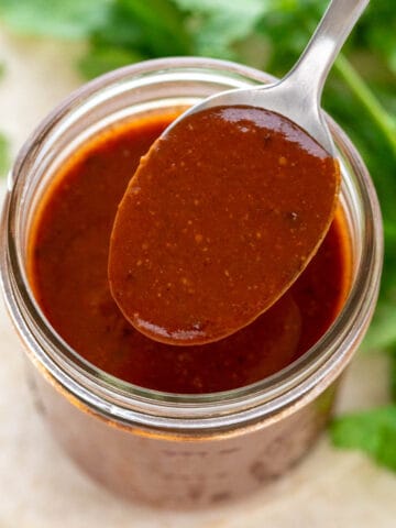 Spoonful of red enchilada sauce resting on a jar of red enchilada sauce.
