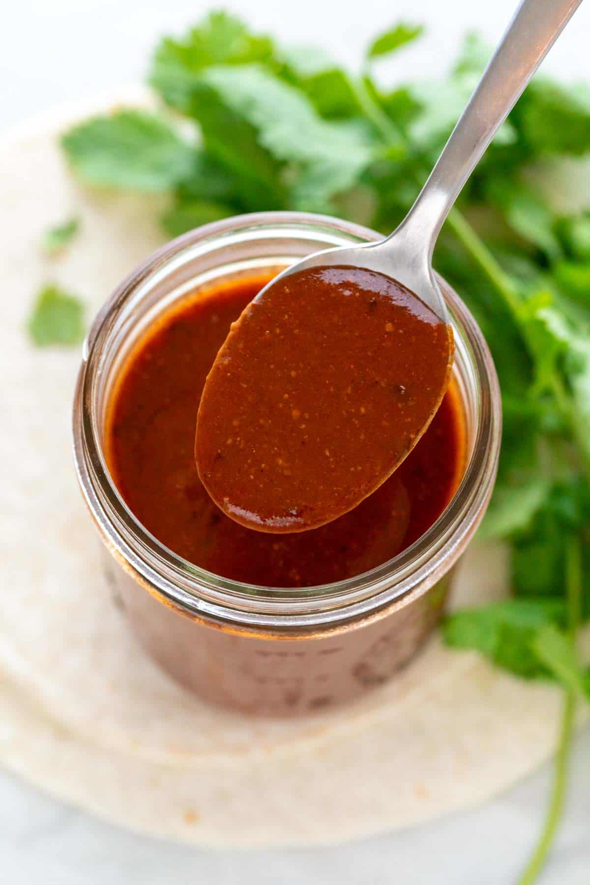 A spoon with red enchilada sauce on top of a red enchilada sauce jar.