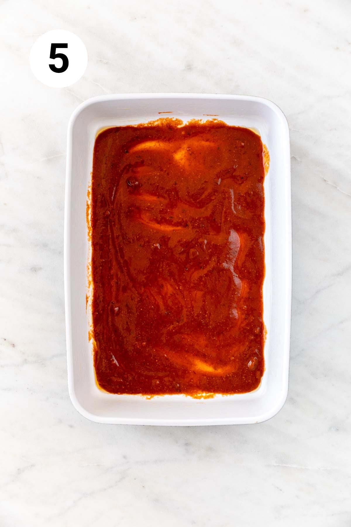 Baking dish with enchilada sauce, evenly spread.