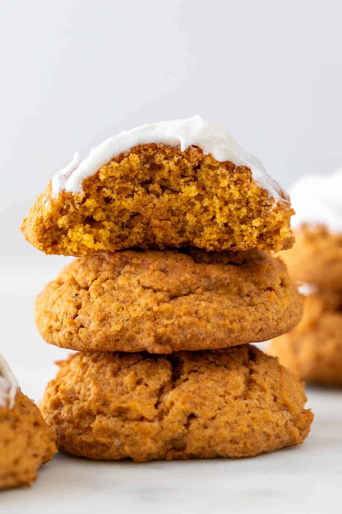 Three vegan pumpkin cookies in a stack, with the top one frosted and a bite missing.