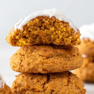 Stack of 3 vegan pumpkin cookies, top one frosted with a bite taken.