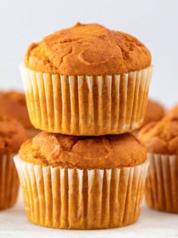 Stacked vegan pumpkin muffins with more muffins in the background.