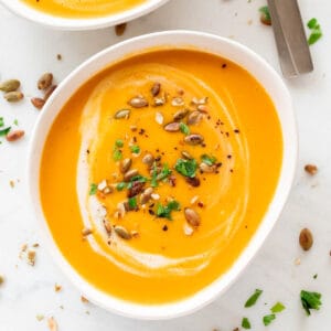 Bowls of vegan pumpkin soup, topped with coconut milk, parsley, and a dash of black pepper.