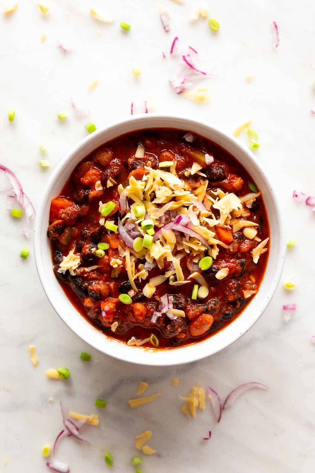 Chili bowl adorned with green onions, red onion, and vegan shredded cheese.