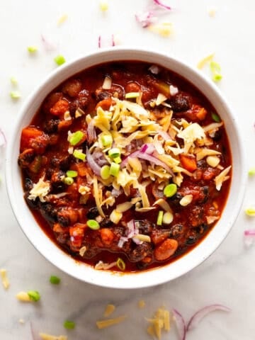 Vegan chili presentation with fresh green onions, red onion, and vegan cheese.