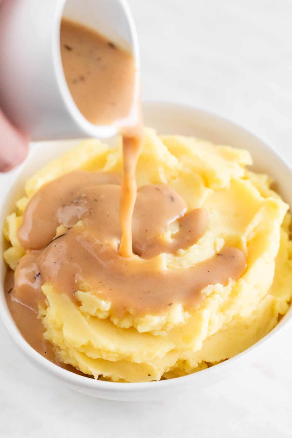 A hand pouring some vegan gravy over a bowl of mashed potatoes.