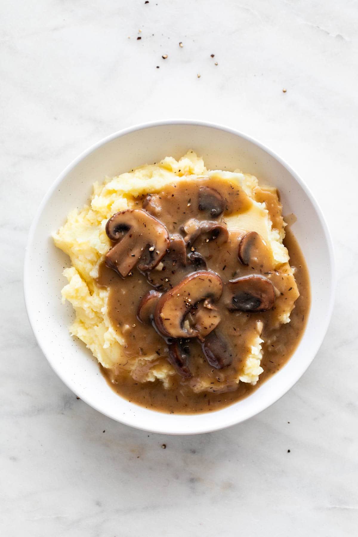 Plate with vegan mashed potatoes and vegan mushroom gravy on a white background.