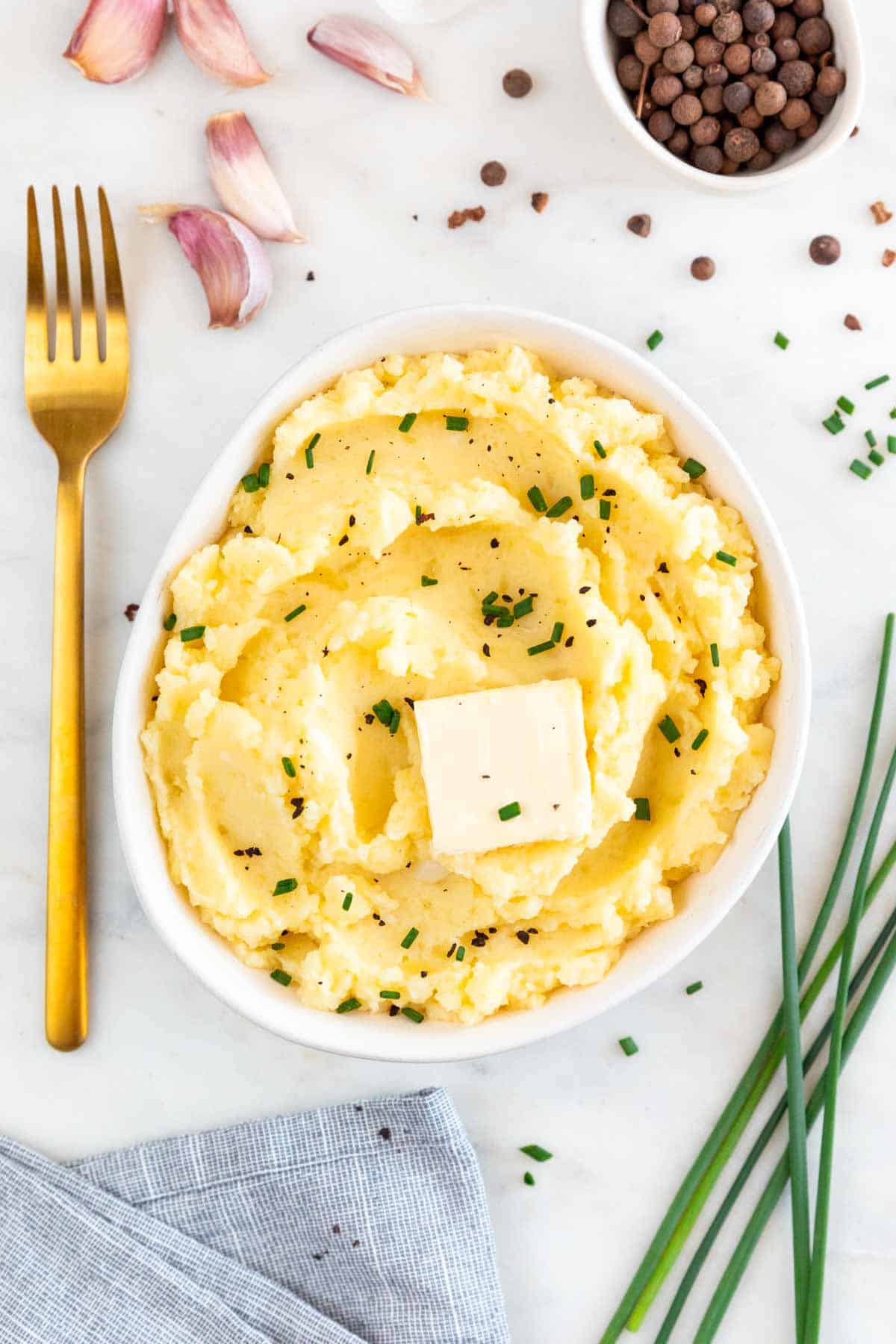Bowl of vegan mashed potatoes garnished with vegan butter, chives, and black pepper.