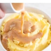 Pouring homemade vegan gravy onto a bowl of creamy mashed potatoes.