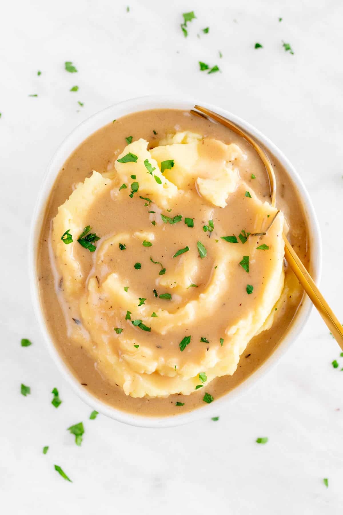 Bowl with mashed potatoes and vegan gravy garnished with parsley and a spoon.