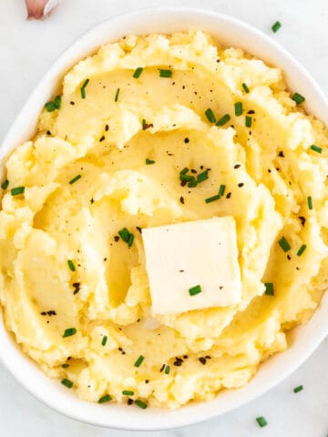 Bowl of vegan mashed potatoes with vegan butter, chives, and black pepper garnish and a fork.