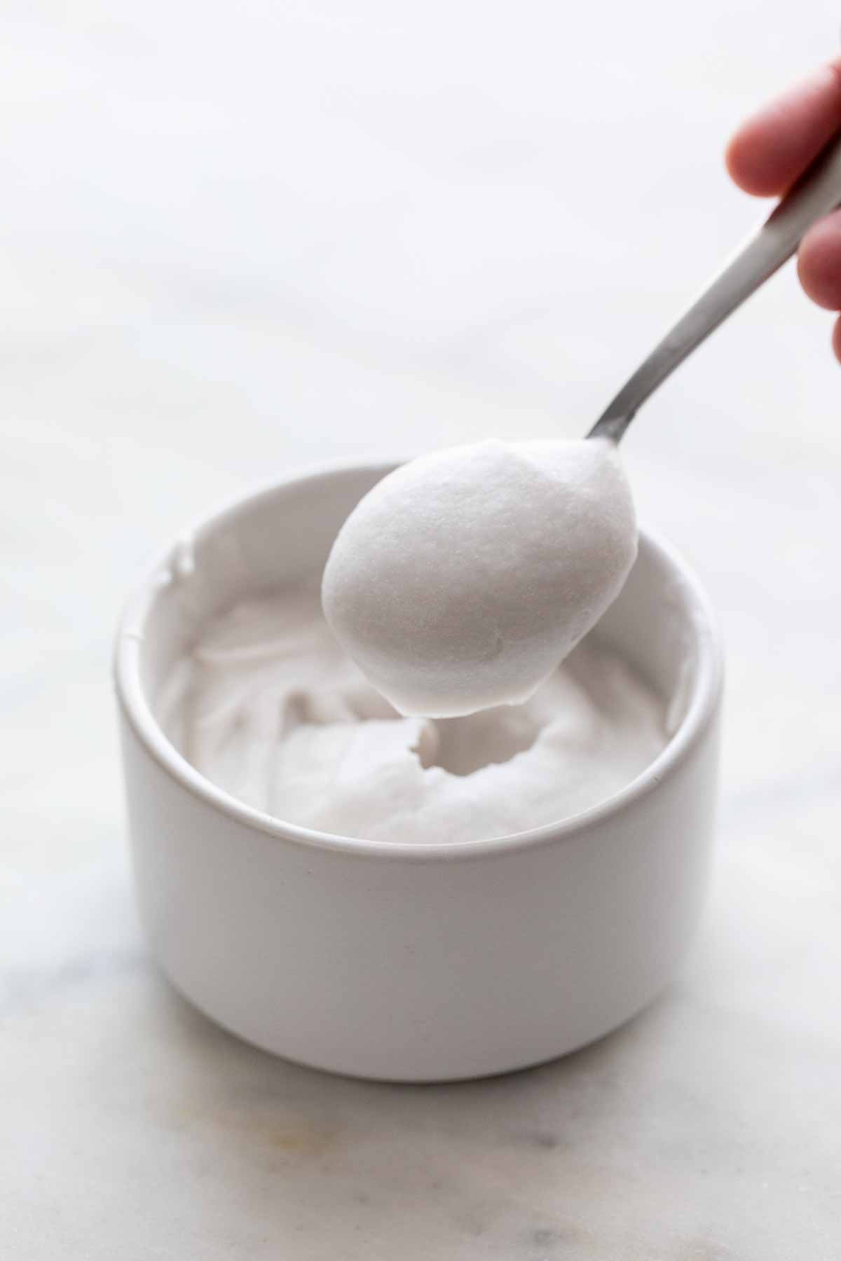 Spoon scooping vegan whipped cream from a bowl.
