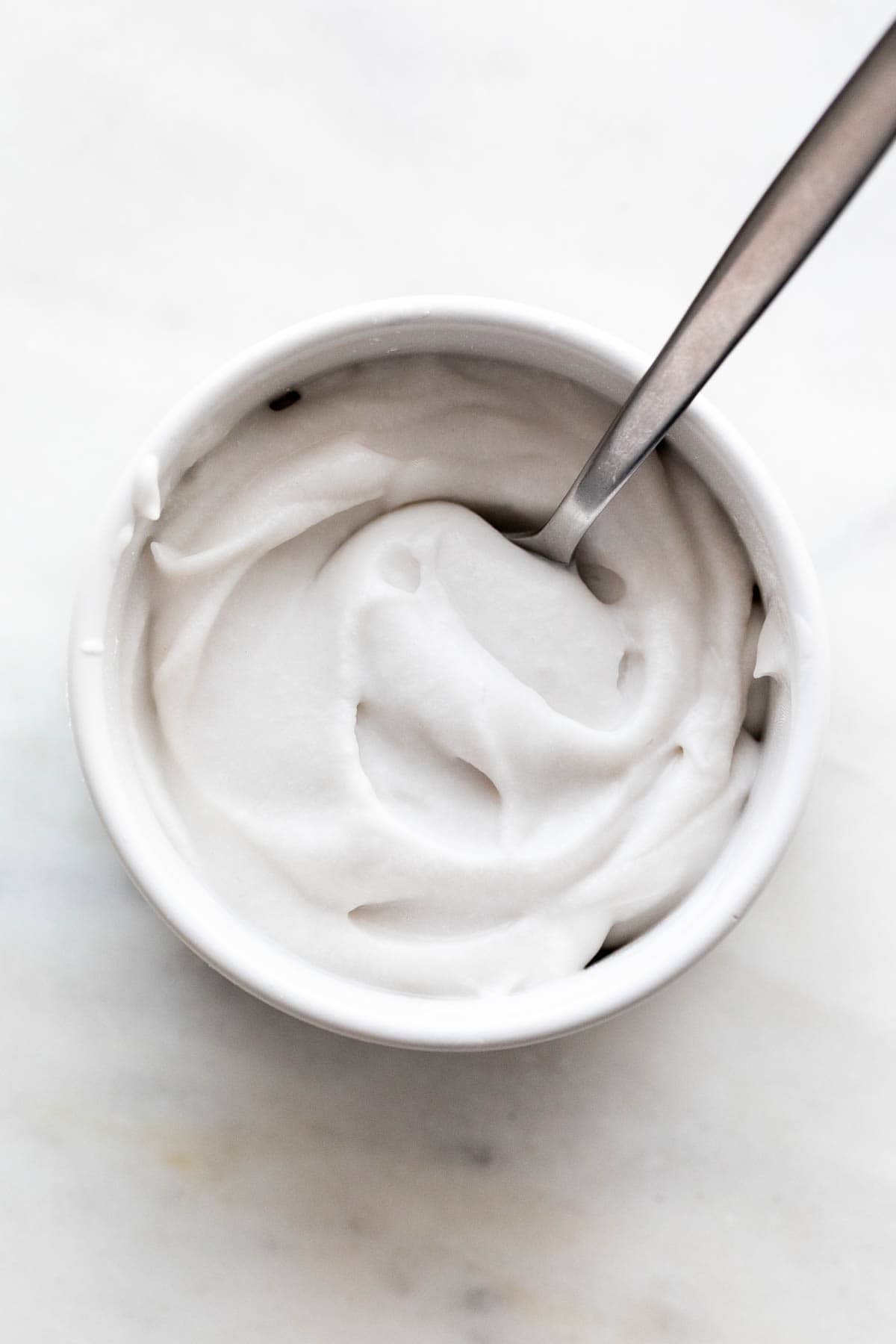 Vegan whipped cream in a bowl with a spoon submerged.