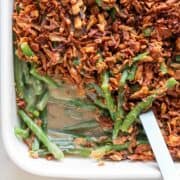 Baking dish of vegan green bean casserole with a serving spoon.