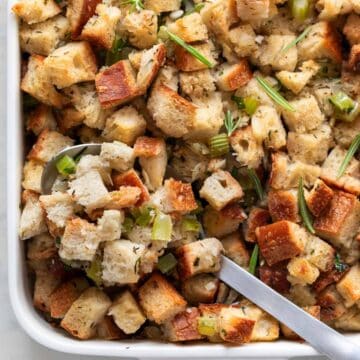 Baked vegan stuffing in a baking dish with a spoon.
