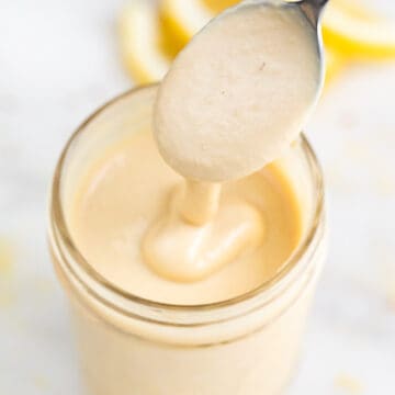 Jar filled with lemon tahini dressing, being spoon-drizzled.